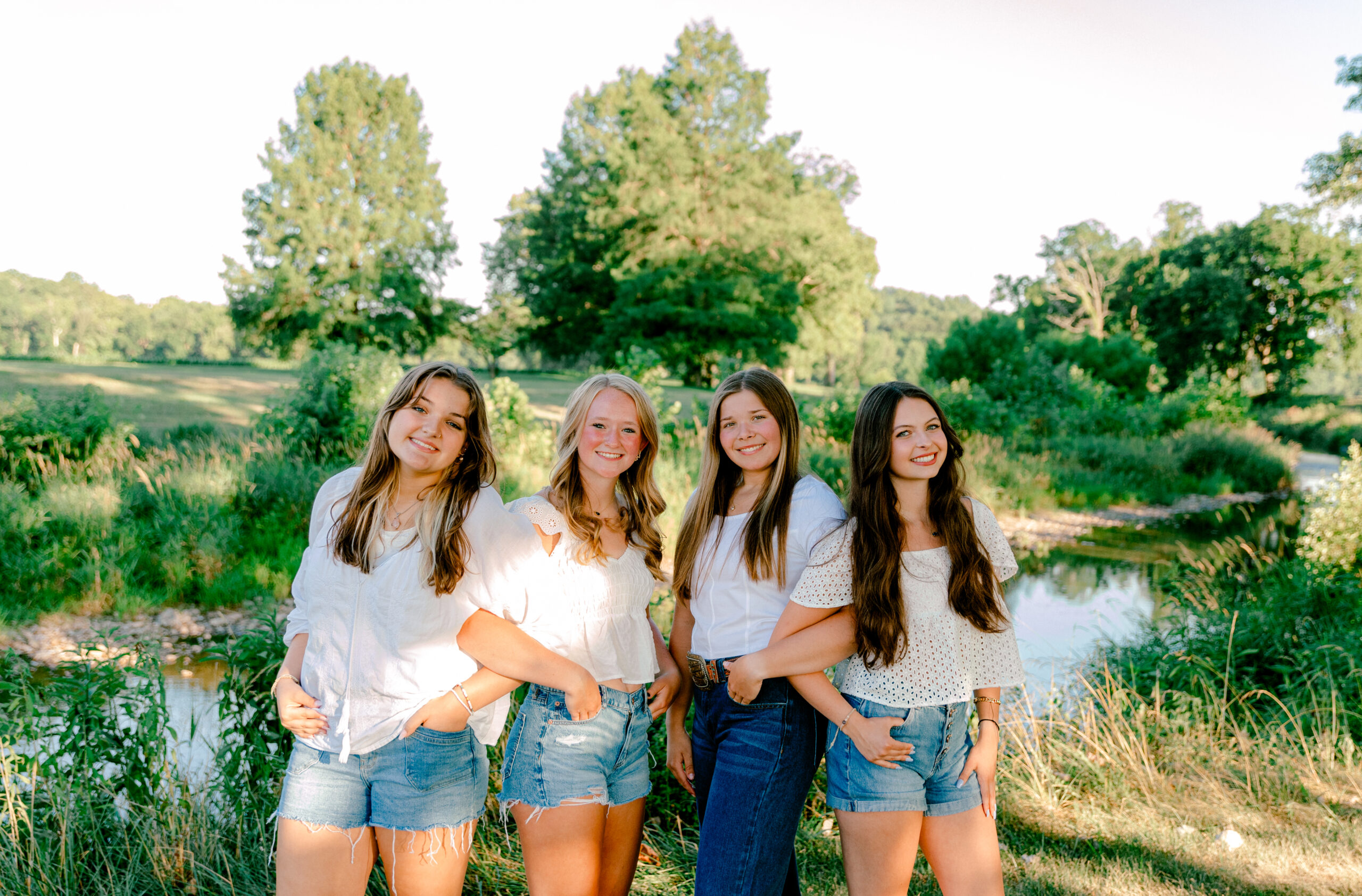 A group of high school seniors from Team 26 posing together outdoors in Virginia, dressed in stylish outfits, laughing and having fun during their senior photography session. Capturing their unique personalities and friendship in a natural, golden-hour setting.